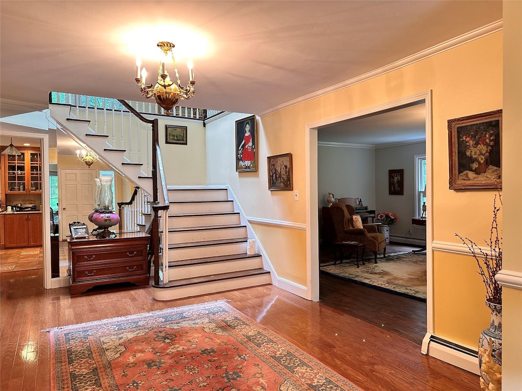 8 Rolling Dr, Brookville, NY 11545 - staircase with a baseboard heating unit, ornamental molding, hardwood / wood-style flooring, and a chandelier