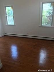 168-03 Cryders Ln, Whitestone, NY 11357 - empty room featuring wood finished floors, plenty of natural light, and a baseboard heating unit