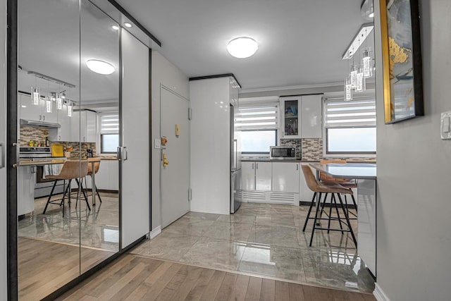 61-45 98th St Unit 11G, Rego Park, NY 11374 - kitchen featuring stainless steel appliances, white cabinets, under cabinet range hood, tasteful backsplash, and crown molding