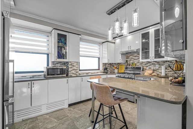 61-45 98th St Unit 11G, Rego Park, NY 11374 - kitchen featuring appliances with stainless steel finishes, under cabinet range hood, ornamental molding, white cabinetry, and a peninsula