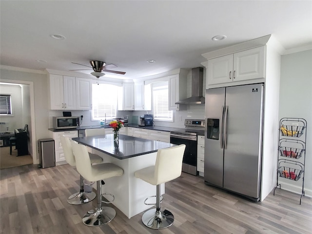 1336 Coates Ave, Holbrook, NY 11741 - kitchen featuring stainless steel appliances, wall chimney range hood, ornamental molding, light wood-type flooring, and white cabinets