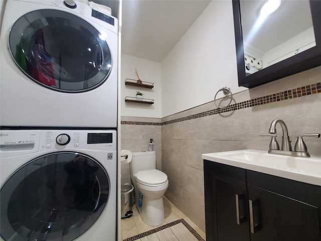 1336 Coates Ave, Holbrook, NY 11741 - laundry room featuring stacked washing machine and dryer, light tile patterned floors, tile walls, and a wainscoted wall