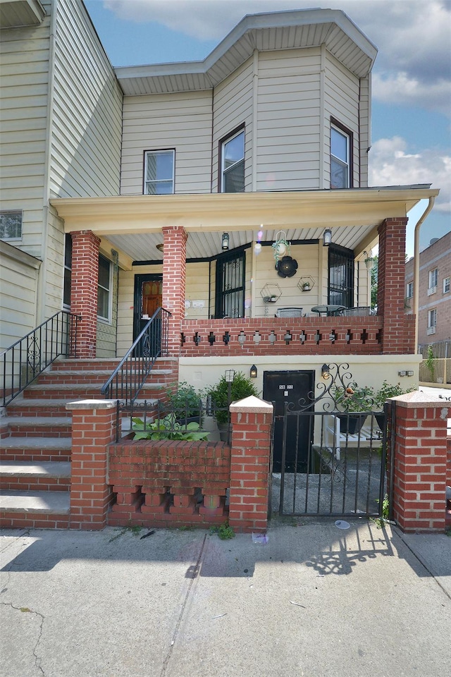 5822 Penrod St, Corona, NY 11368 - view of front facade featuring a fenced front yard, stairway, covered porch, a gate, and brick siding