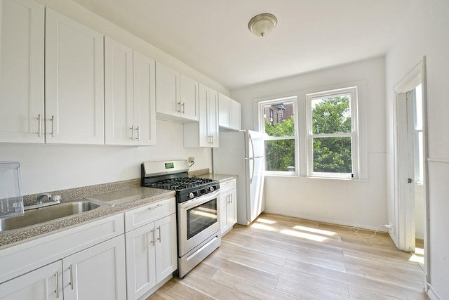 5822 Penrod St, Corona, NY 11368 - kitchen featuring stainless steel gas stove, freestanding refrigerator, white cabinetry, and light wood-style floors