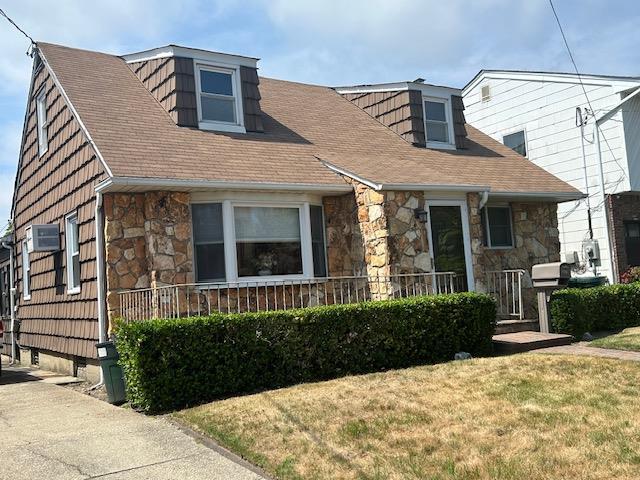 862 Peninsula Blvd, Woodmere, NY 11598 - new england style home with stone siding, a front yard, an AC wall unit, and a shingled roof