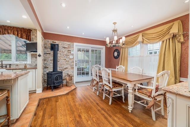 11 Loel Ct, Rockville Centre, NY 11570 - dining area with a chandelier, a wood stove, light wood-style floors, and ornamental molding