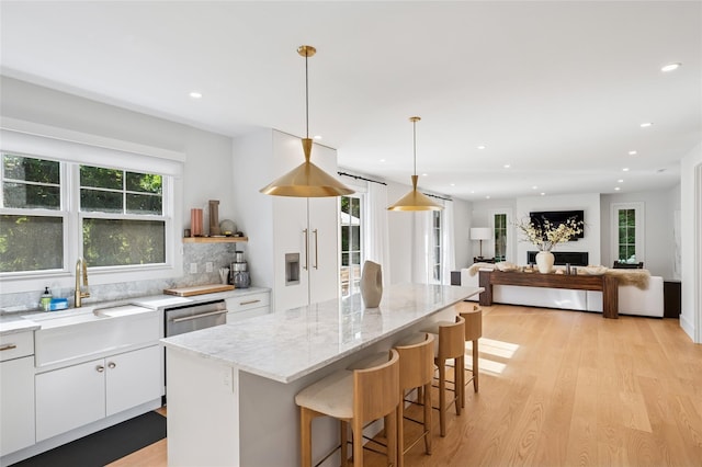 5 Kings Ln, Southampton, NY 11968 - kitchen with light wood-type flooring, a kitchen bar, a kitchen island, white cabinets, and light stone counters