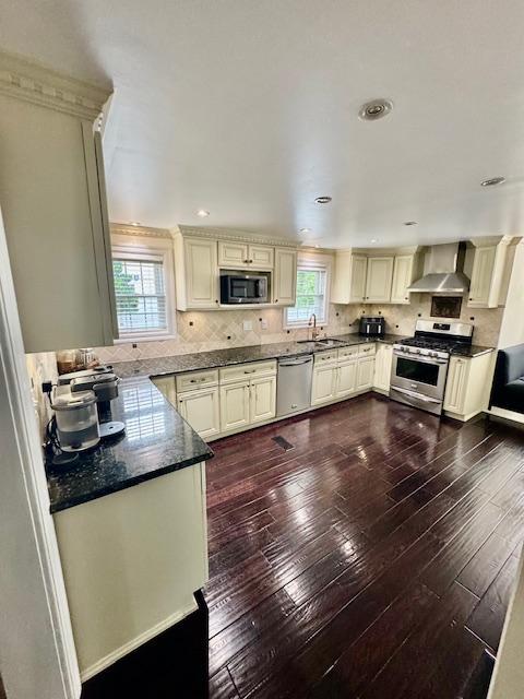 987 E Prospect St, Woodmere, NY 11598 - kitchen featuring appliances with stainless steel finishes, wall chimney range hood, cream cabinets, plenty of natural light, and recessed lighting