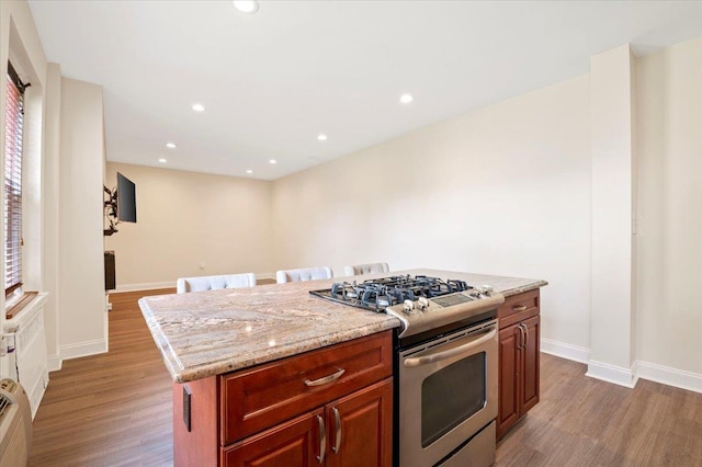 819 Broadway Unit 1G, Woodmere, NY 11598 - kitchen with stainless steel range with gas stovetop, wood finished floors, a center island, recessed lighting, and light stone counters