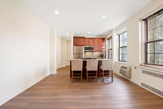 819 Broadway Unit 1G, Woodmere, NY 11598 - kitchen featuring appliances with stainless steel finishes, radiator, a breakfast bar, a wall mounted air conditioner, and brown cabinetry
