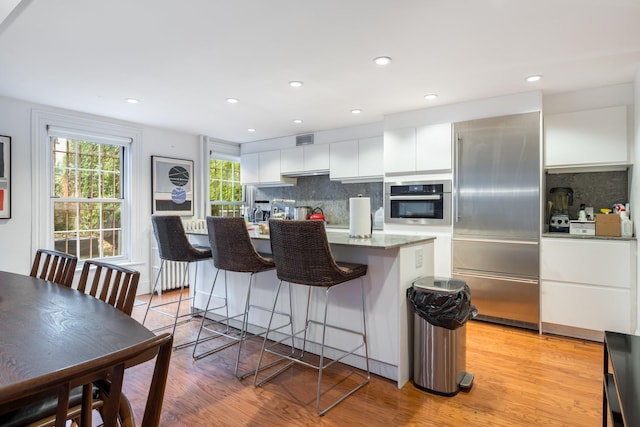 17E 128th St, New York Manhattan, NY 10035 - kitchen with stainless steel appliances, a kitchen island, decorative backsplash, white cabinetry, and a kitchen breakfast bar