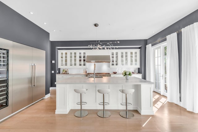 7 Honeysuckle Ln, Rye Brook, NY 10573 - kitchen featuring light wood finished floors, white cabinetry, light countertops, glass insert cabinets, and custom exhaust hood