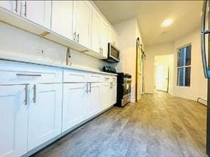 130 W 165th St, Bronx, NY 10452 - kitchen with appliances with stainless steel finishes, white cabinetry, and wood finished floors