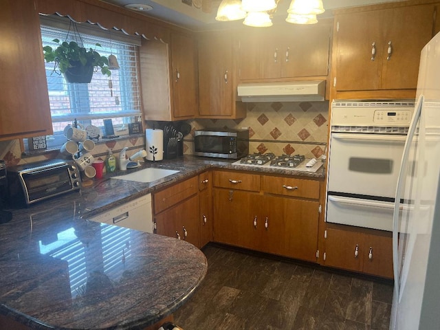 15916 92nd St, Howard Beach, NY 11414 - kitchen featuring white appliances, under cabinet range hood, a warming drawer, tasteful backsplash, and brown cabinetry
