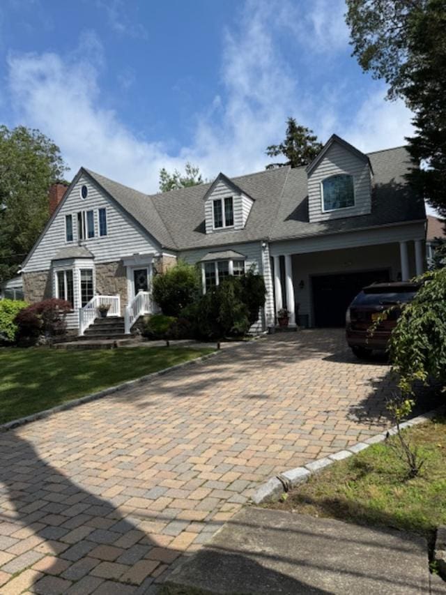 9 Seneca St E, Massapequa, NY 11758 - cape cod-style house with decorative driveway, stone siding, a garage, a shingled roof, and a chimney