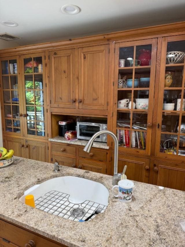 9 Seneca St E, Massapequa, NY 11758 - kitchen featuring brown cabinetry, light stone counters, glass insert cabinets, and recessed lighting