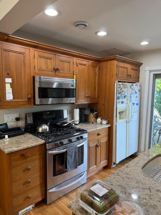 9 Seneca St E, Massapequa, NY 11758 - kitchen with stainless steel appliances, brown cabinets, light wood-type flooring, light stone counters, and recessed lighting