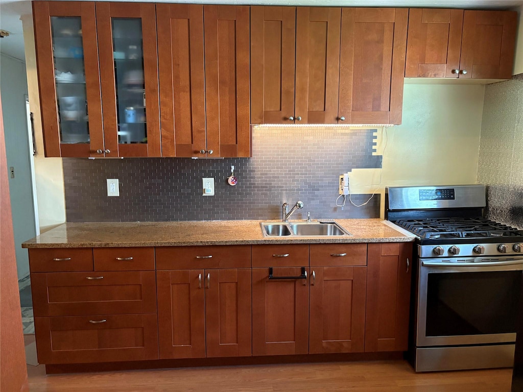 6 Poplar Rd, Amityville, NY 11701 - kitchen with stainless steel range with gas stovetop, brown cabinetry, light wood-type flooring, tasteful backsplash, and glass insert cabinets