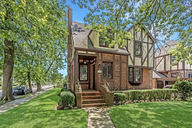 25 Reyam Rd, Lynbrook, NY 11563 - tudor-style house featuring a front lawn, brick siding, and roof with shingles