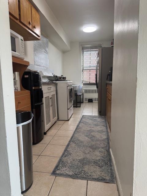 83-30 Vietor Ave Unit 716, Elmhurst, NY 11373 - kitchen with white appliances, radiator, light tile patterned floors, and brown cabinets