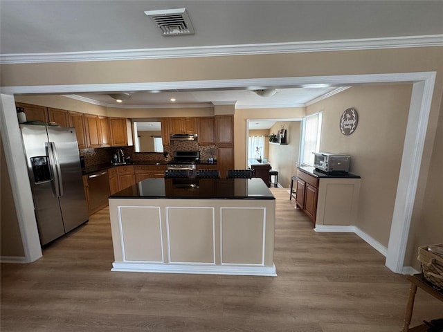 3805 Mansfield Dr, Seaford, NY 11783 - kitchen with appliances with stainless steel finishes, dark countertops, brown cabinets, a kitchen island, and light wood finished floors