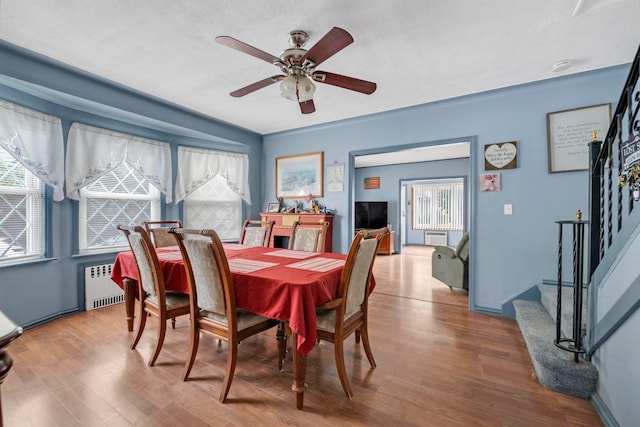 7609 79th St, Glendale, NY 11385 - dining room featuring radiator, wood finished floors, ceiling fan, and stairs