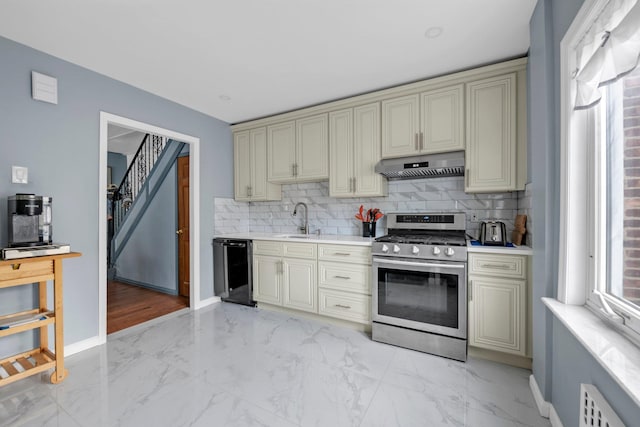 7609 79th St, Glendale, NY 11385 - kitchen featuring stainless steel gas stove, cream cabinetry, under cabinet range hood, and light marble finish floors