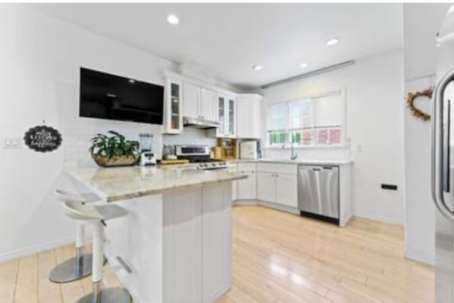 39-12 215th Pl, Bayside, NY 11362 - kitchen featuring a peninsula, white cabinets, a breakfast bar area, glass insert cabinets, and light wood-style flooring