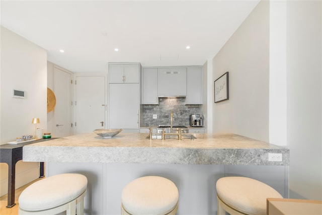 250 E 21st St Unit 9D, New York Manhattan, NY 10010 - kitchen featuring tasteful backsplash, a peninsula, a breakfast bar, gray cabinetry, and light countertops