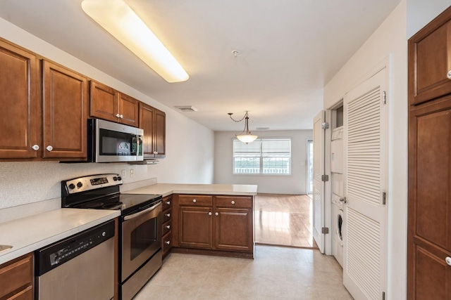 117 Willow Ln, Valley Stream, NY 11580 - kitchen featuring stainless steel appliances, a peninsula, stacked washer / drying machine, light countertops, and brown cabinets