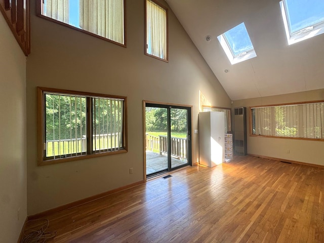 unfurnished living room with high vaulted ceiling, a skylight, plenty of natural light, and wood finished floors