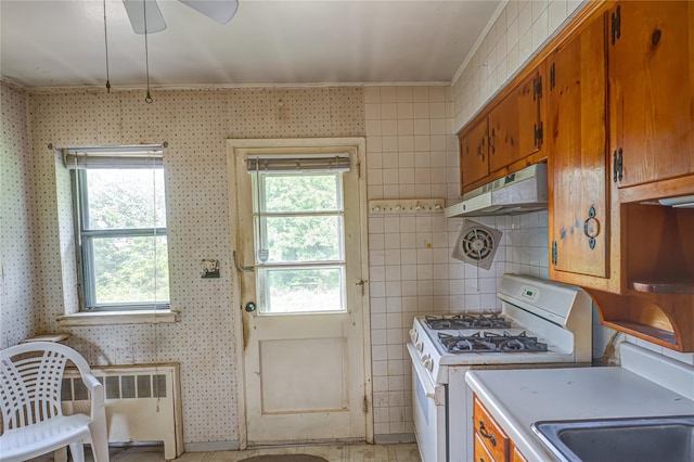 1435 Peters Blvd, Bay Shore, NY 11706 - kitchen featuring white gas stove, brown cabinets, under cabinet range hood, crown molding, and a ceiling fan