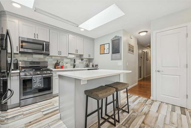 76 Cadman Ave, Babylon, NY 11702 - kitchen featuring appliances with stainless steel finishes, light countertops, a breakfast bar, decorative backsplash, and recessed lighting