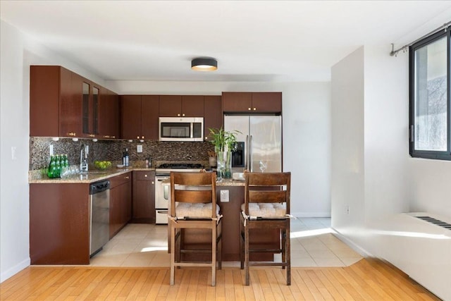 2287 Johnson Ave Unit 3A, Bronx, NY 10463 - kitchen with appliances with stainless steel finishes, light wood finished floors, tasteful backsplash, a kitchen breakfast bar, and dark brown cabinetry