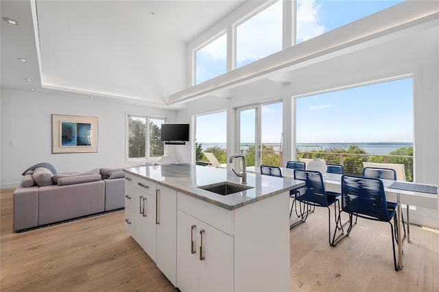 846 Dune Rd, Westhampton Dunes, NY 11978 - kitchen with light stone countertops, a center island with sink, light wood-style flooring, open floor plan, and a towering ceiling