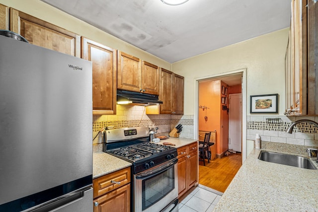 7910 34th Ave Unit 4J, Jackson Heights, NY 11372 - kitchen with appliances with stainless steel finishes, tasteful backsplash, light tile patterned floors, under cabinet range hood, and brown cabinets