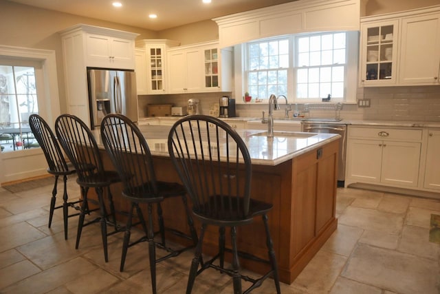 kitchen with a healthy amount of sunlight, appliances with stainless steel finishes, an island with sink, and white cabinets