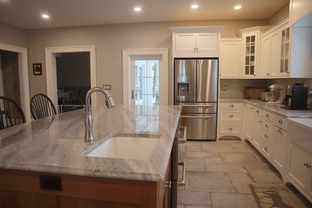 kitchen featuring stainless steel refrigerator with ice dispenser, a breakfast bar, sink, light stone countertops, and white cabinets