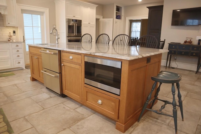 kitchen featuring sink, white cabinetry, appliances with stainless steel finishes, a large island, and light stone countertops