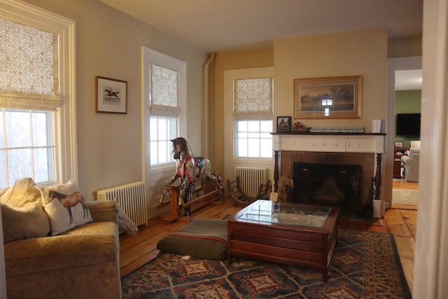 living room featuring radiator, hardwood / wood-style floors, and a brick fireplace