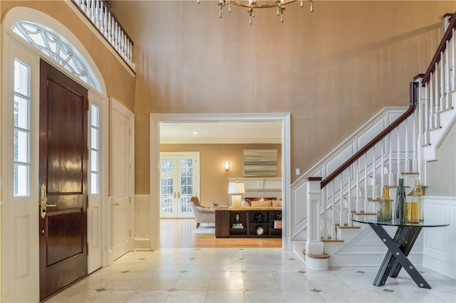 foyer entrance featuring a towering ceiling, crown molding, and french doors