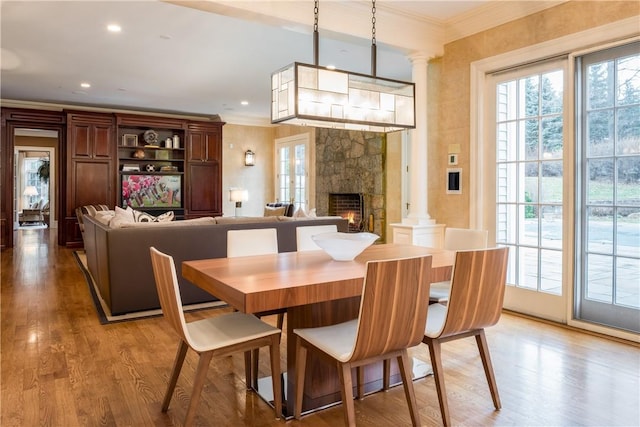 dining room with light hardwood / wood-style flooring, crown molding, a fireplace, and decorative columns