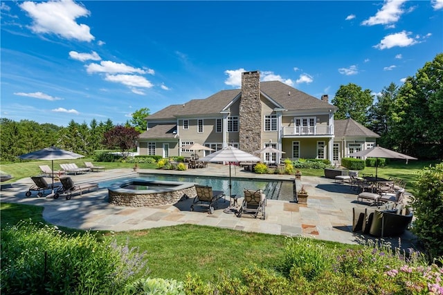 back of property featuring a swimming pool with hot tub, a patio, a balcony, and a yard