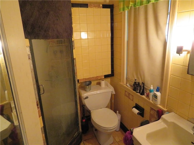 bathroom featuring tile patterned flooring, a shower with door, tile walls, and toilet