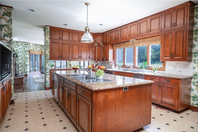 kitchen with sink, dishwasher, hanging light fixtures, light stone counters, and a kitchen island with sink