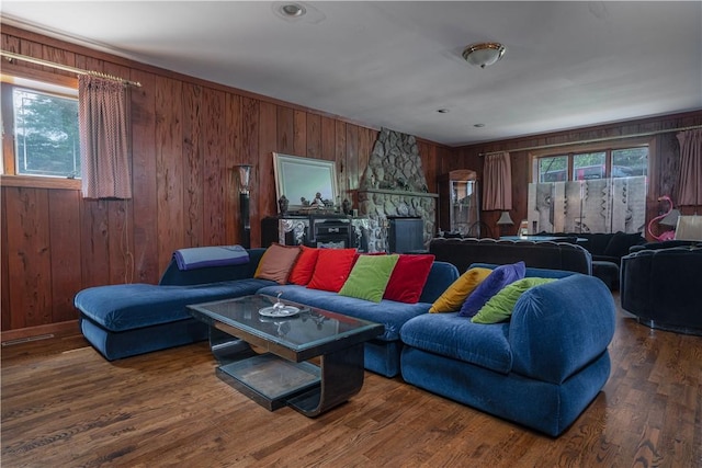 living room with wood walls, dark hardwood / wood-style flooring, and a stone fireplace