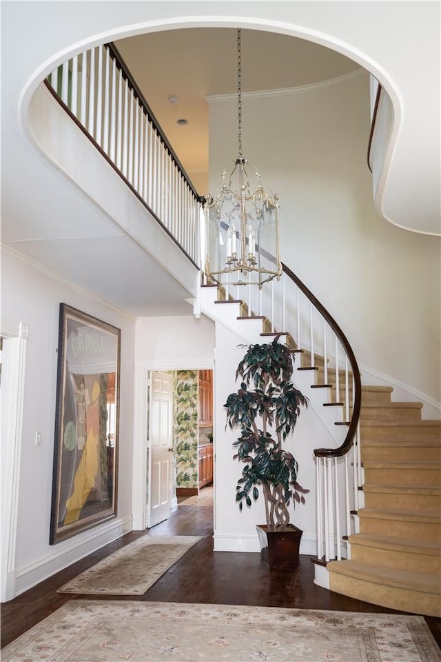 foyer with crown molding, a high ceiling, dark hardwood / wood-style floors, and an inviting chandelier