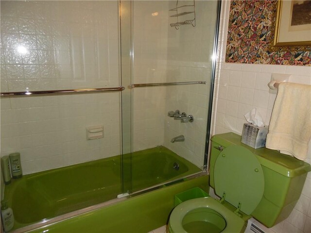 bathroom featuring toilet, a baseboard radiator, tile walls, and combined bath / shower with glass door