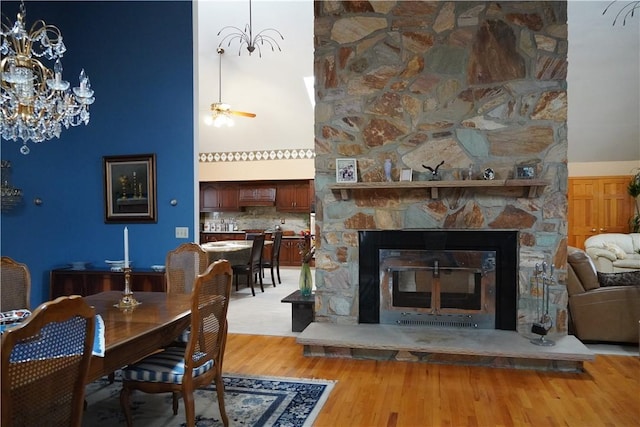 dining space with a towering ceiling, light hardwood / wood-style flooring, a stone fireplace, and ceiling fan