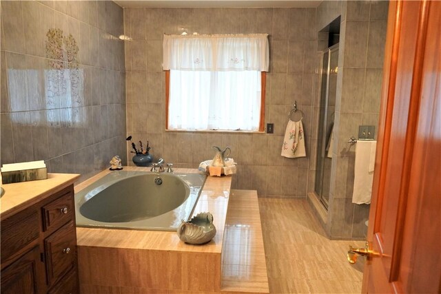 bathroom featuring plus walk in shower, vanity, and tile walls